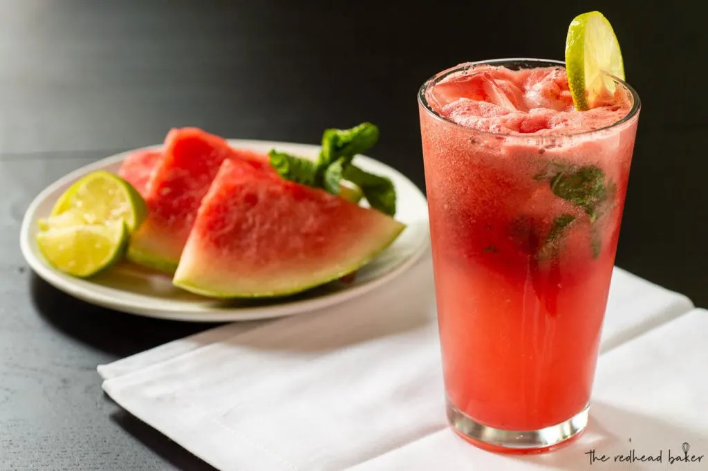 A watermelon coconut mojito in front of a plate of watermelon wedges