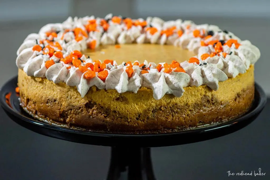 A pumpkin cheesecake with gingersnap crust and spiced whipped cream on a black cake stand
