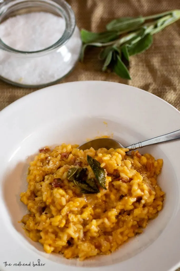 A tablescape with a dish of pumpkin pancetta risotto, a dish of salt and fresh sage leaves