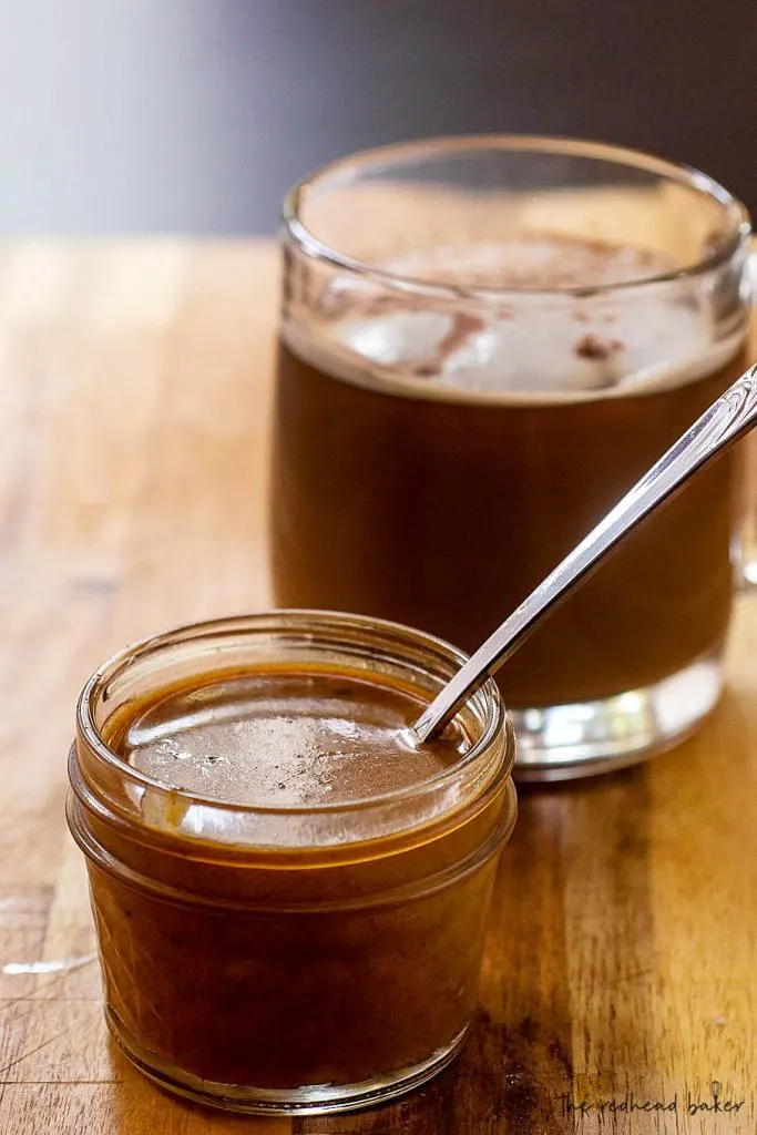 A jar of pumpkin white chocolate mocha sauce in front of a cup of coffee