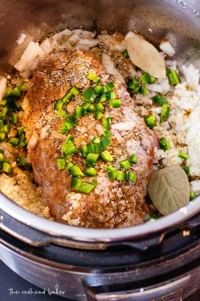 A piece of pork shoulder with diced onion and jalapeno in an Instant Pot