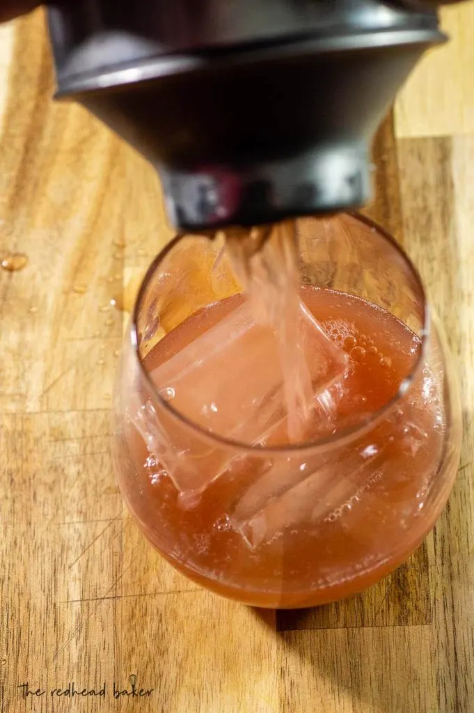 Pomegranate ginger whiskey sour being poured into a glass with ice