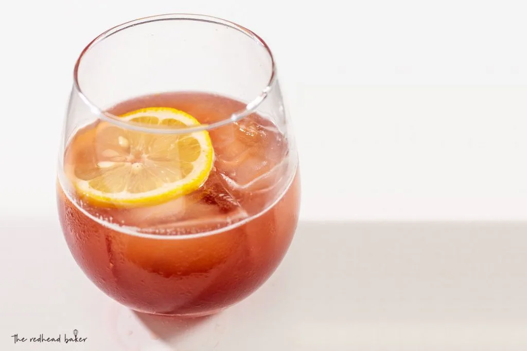 A glass of pomegranate ginger whiskey sour on a white background