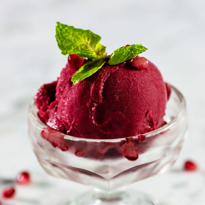 A dish of pomegranate sorbet garnished with pomegranate seeds and a sprig of mint.