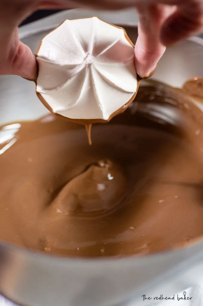 A meringue cookie being dipped in melted milk chocolate