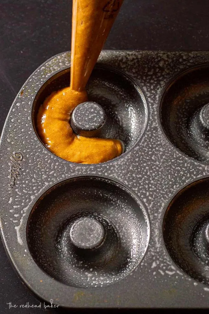 A donut pan being filled with baked gingerbread donut batter