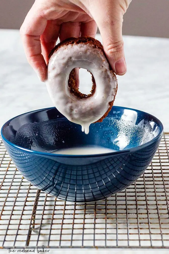 A baked gingerbread donut being dipped in maple icing