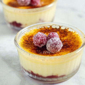 Two ramekins of cranberry creme brulee topped with sugared cranberries.