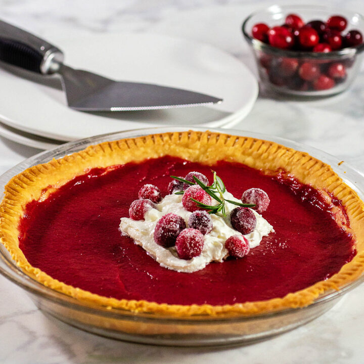 Cranberry curd pie topped with whipped cream and sugared cranberries.