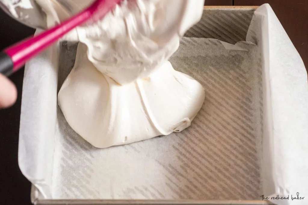 Marshmallow being scraped into a parchment-lined pan