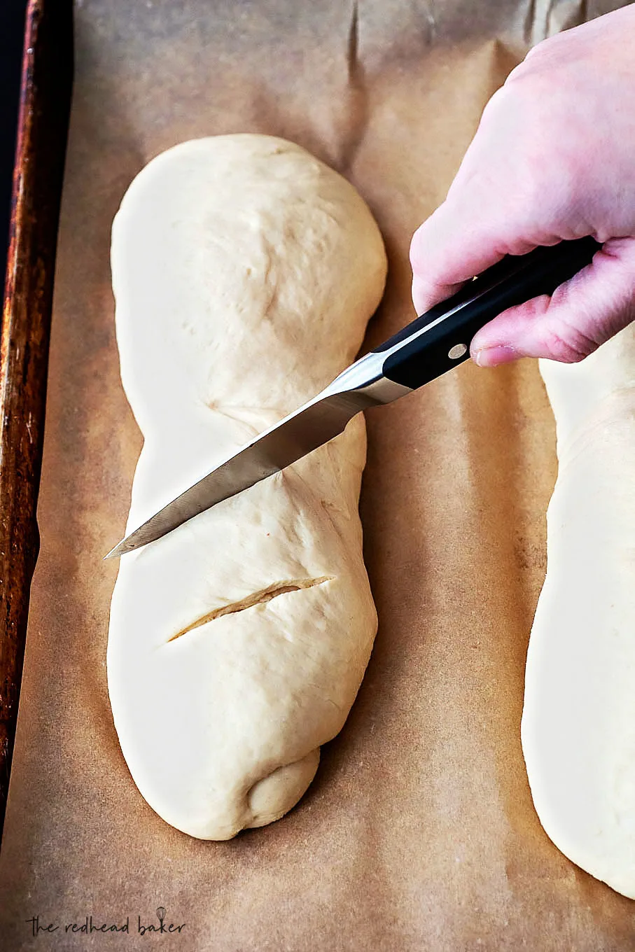 A loaf of bread being scored with a parking knife.