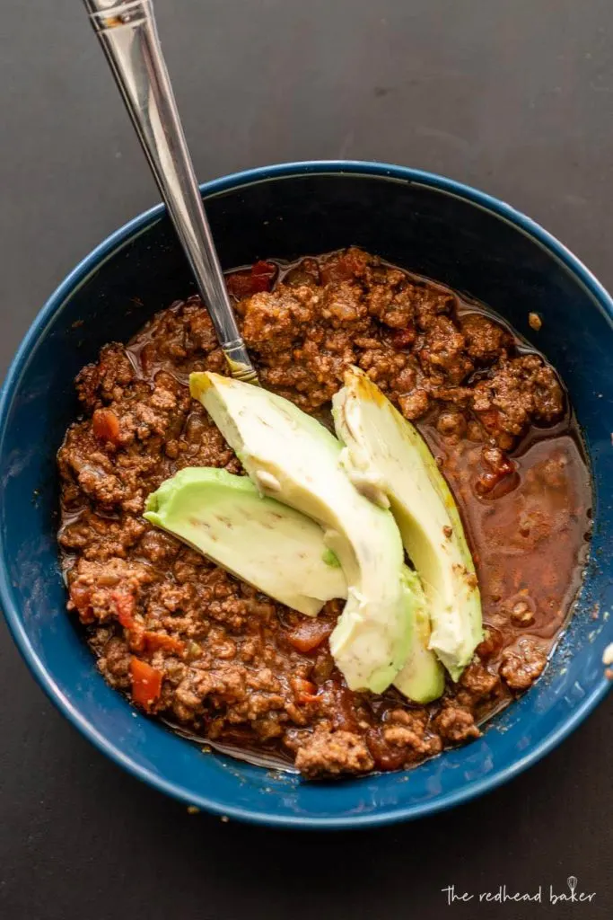 An overhead view of a bowl of beef chili garnished with avocado slices