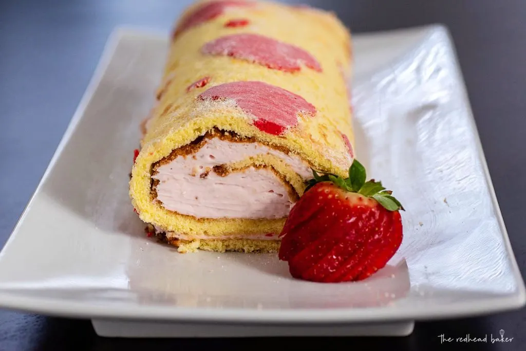 A straight-on view of a strawberry cake roll on a white serving plate