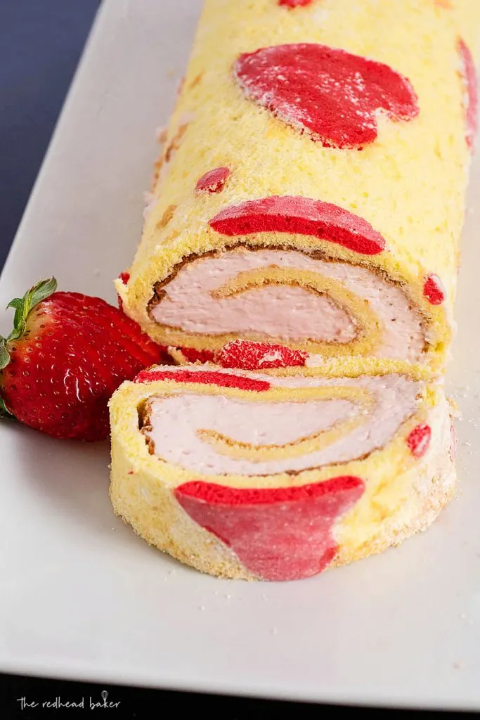 A close-up view of a strawberry jelly roll cake with one slice cut off and laying on its side
