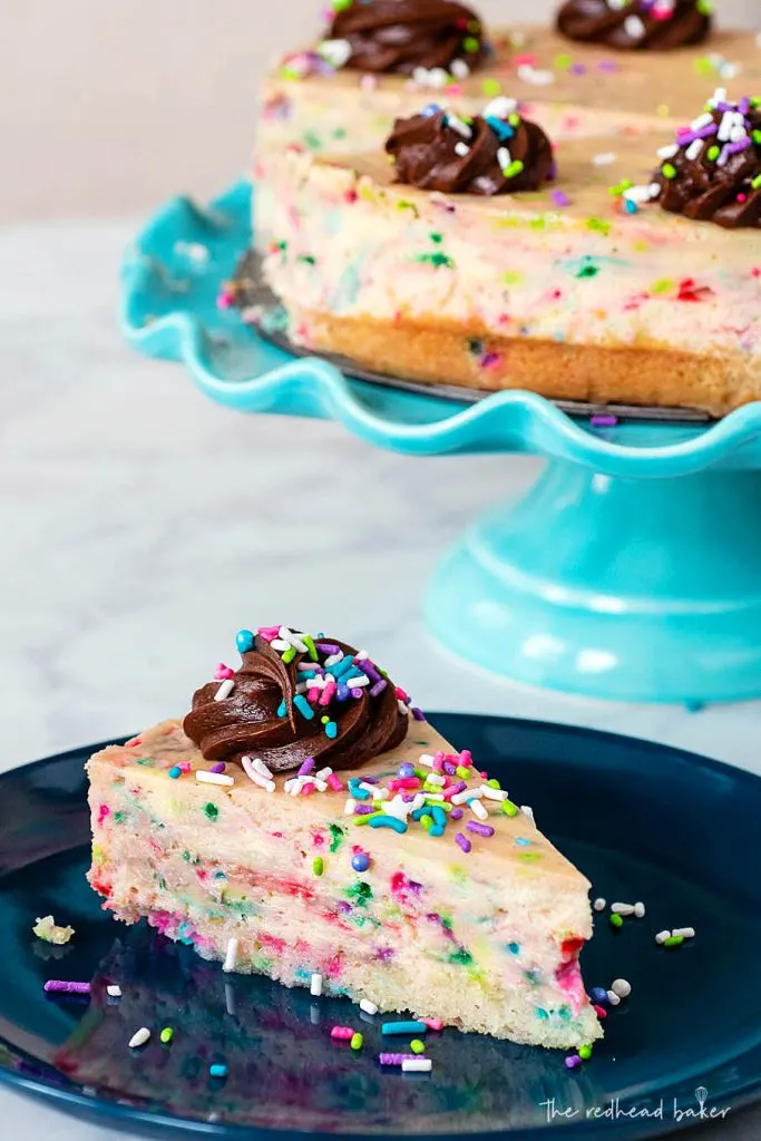 A slice of cheesecake on a blue plate in front of a blue cake stand