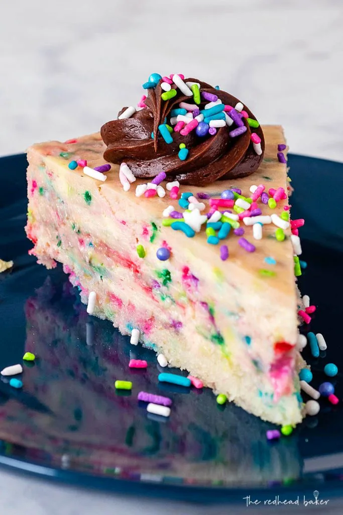 A close-up of a slice of cheesecake topped with frosting and sprinkles