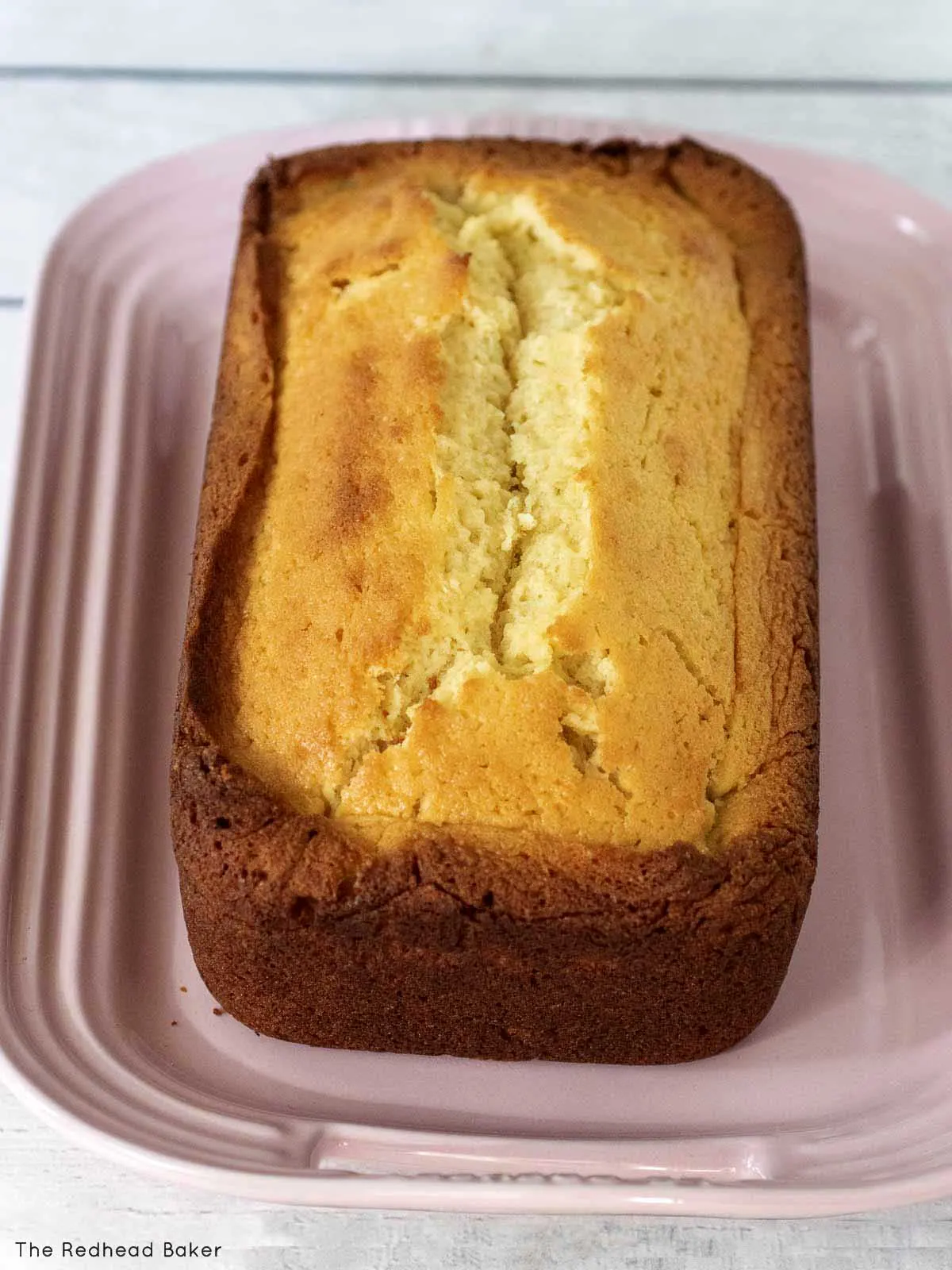 An unglazed pound cake on a pink serving tray.