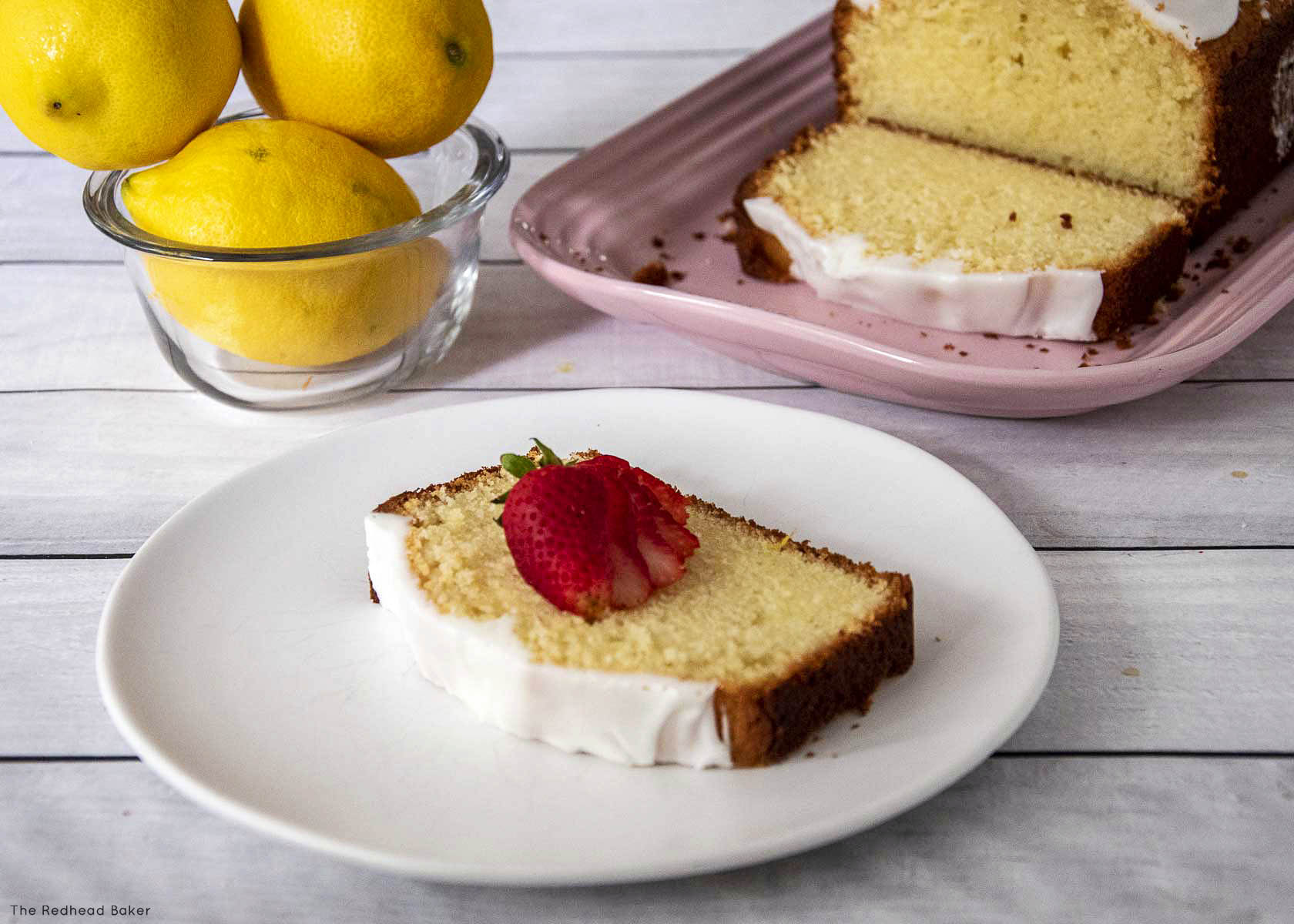 A slice of pound cake on a white plate topped with a strawberry.