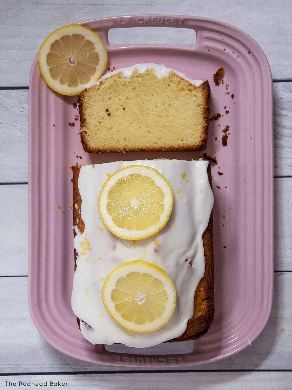 An overhead view of a pound cake on a pink serving tray with one cut slice laying down.