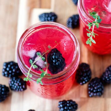 An overhead view of a glass of blackberry thyme collins garnished with thyme and fresh blackberries