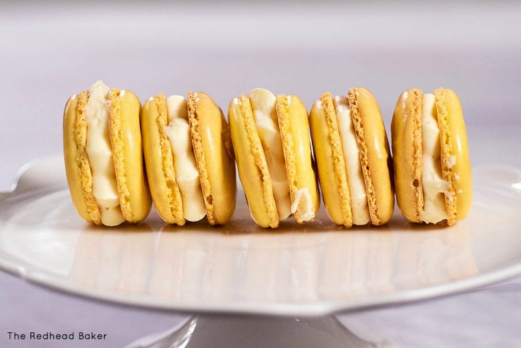 Five lemon macarons on a white cake stand