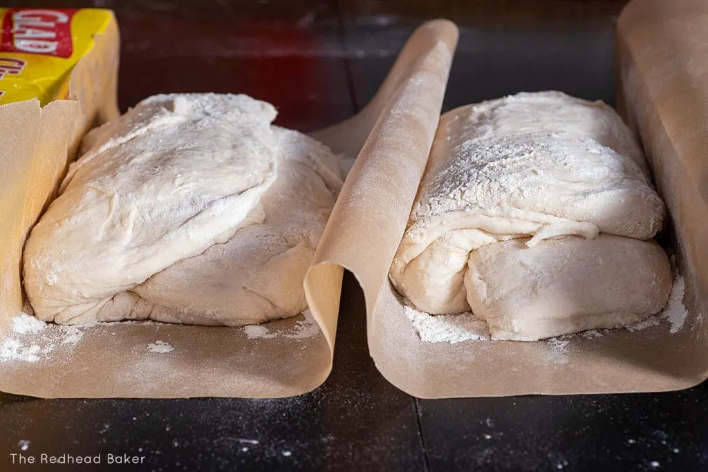 Two loaves of ciabatta proofing in a homemade "couche" made of parchment paper