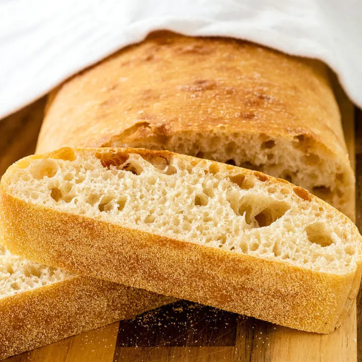 A cut loaf of ciabatta bread with two slices piled in front