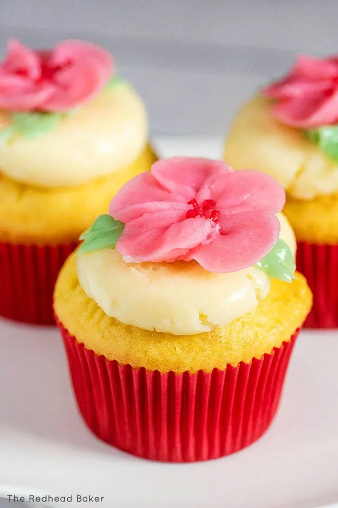 Three cupcakes frosted with swiss buttercream and topped with buttercream cherry blossoms