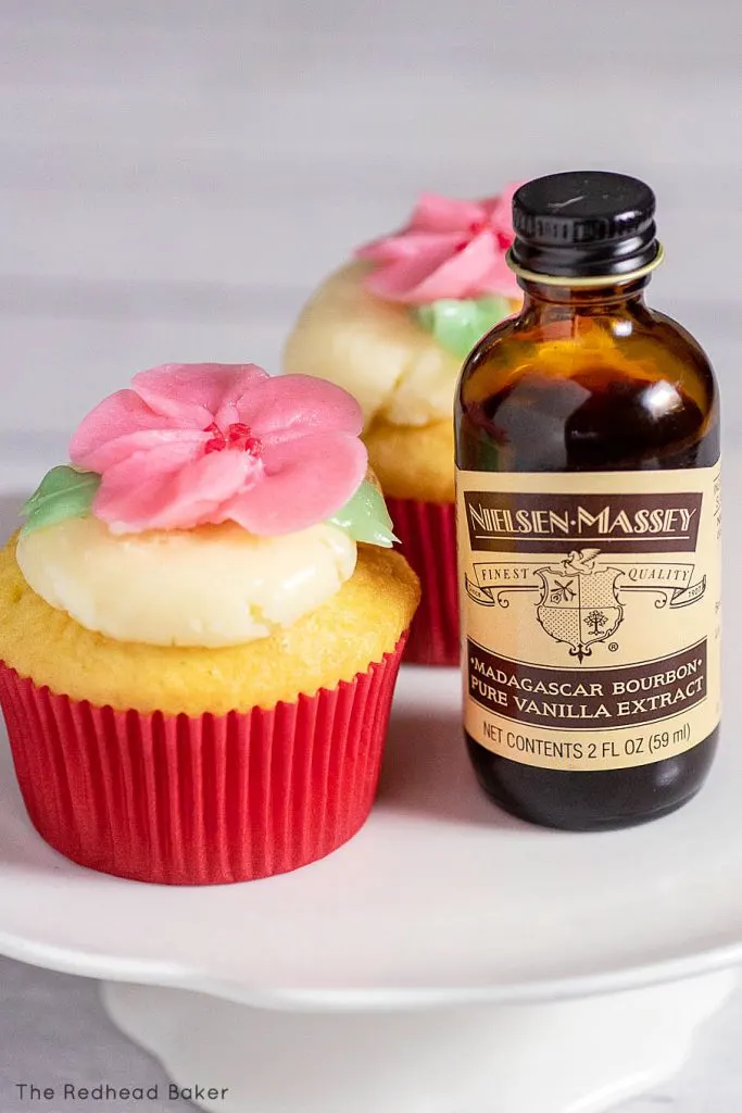 Two cupcakes next to a bottle of Nielsen-Massey vanilla extract