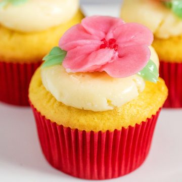 A vanilla cupcake iced with swiss buttercream and topped with a buttercream cherry blossom