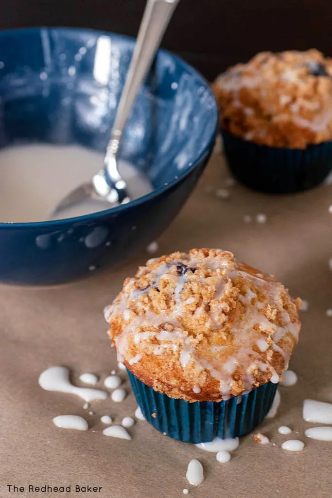 Two muffins next to a bowl of confectioners sugar glaze