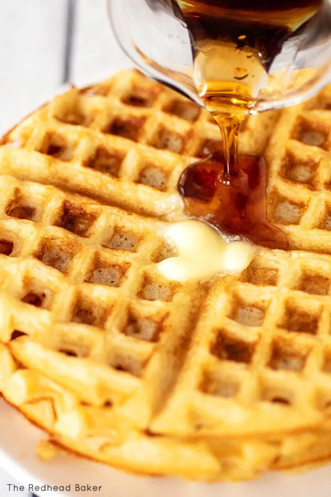 A close-up of maple syrup being poured over waffles