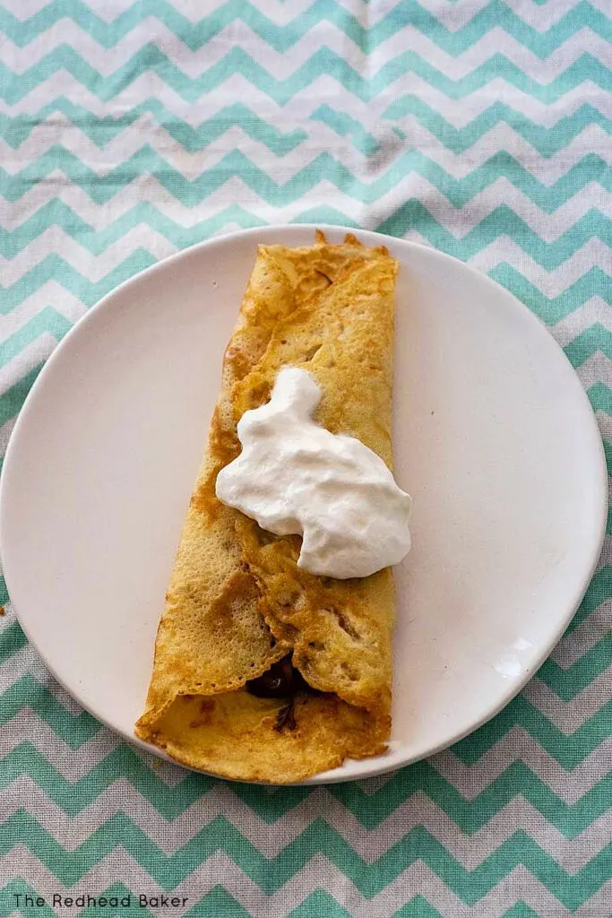 A filled rolled crepe topped with whipped cream