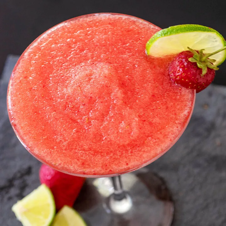 A frozen strawberry daiquiri garnished with a fresh strawberry and a lime slice