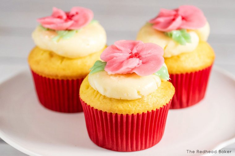 Three cupcakes frosted with swiss buttercream and topped with buttercream cherry blossoms