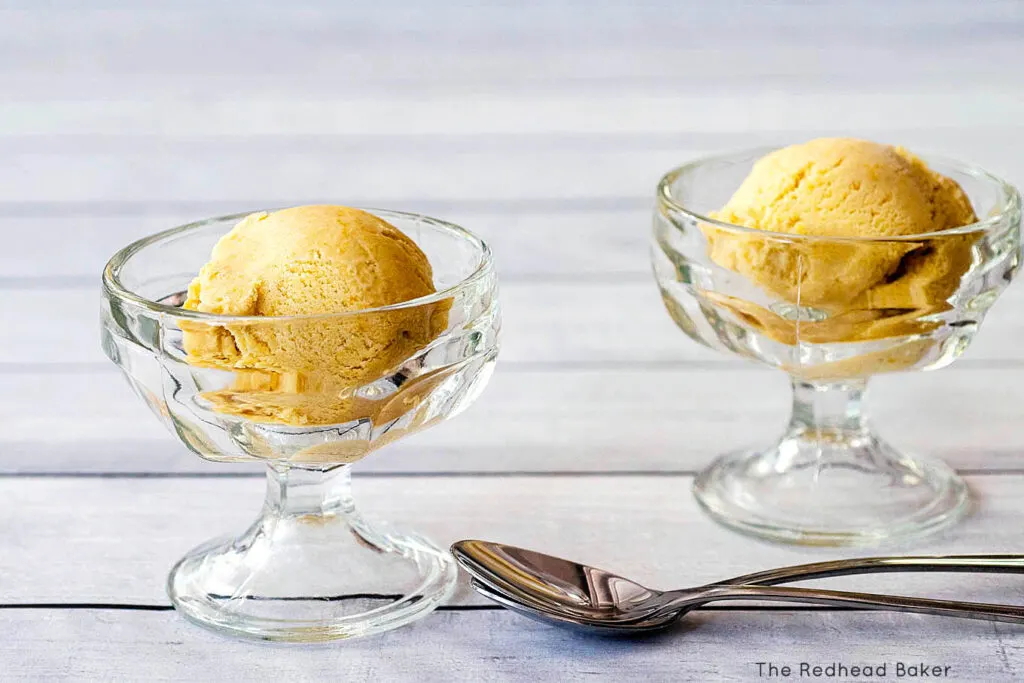 Two glass dishes of peach ice cream with two long spoons