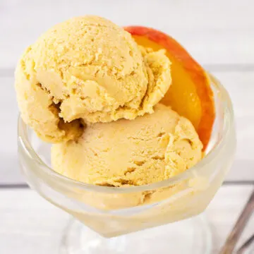 A close-up of two scoops of ice cream in a glass dish with a peach slice