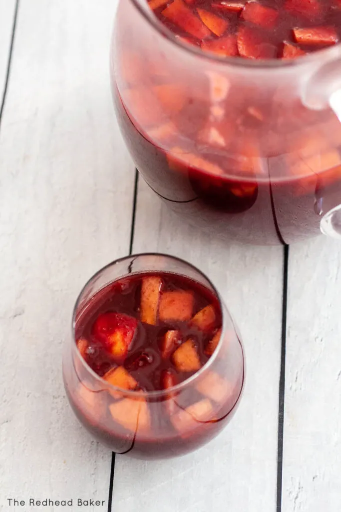 A glass of sangria in front of a pitcher 