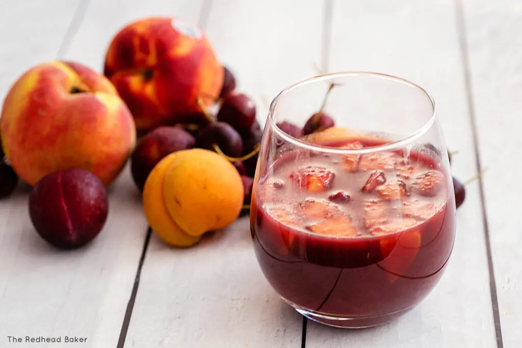 A glass of stone fruit sangria in front of a pile of stone fruits
