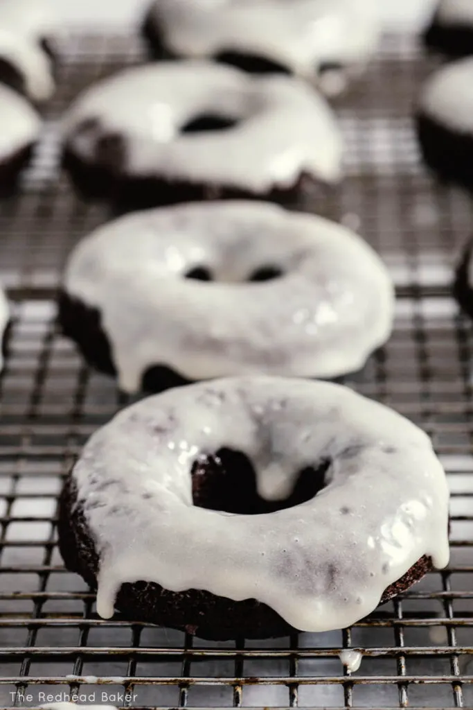 A row of glazed chocolate donuts on a wire rack