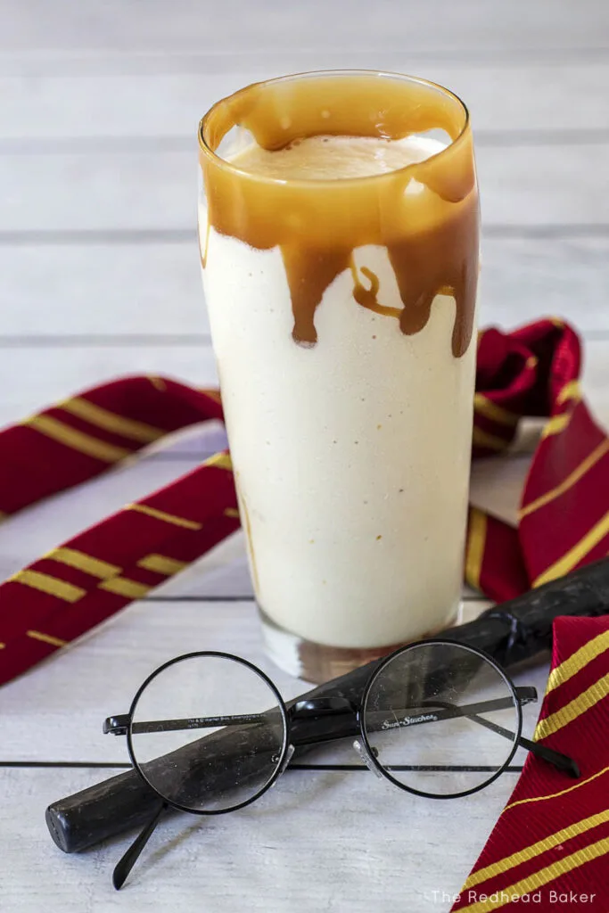 A milkshake with butterscotch sauce dripping down the side behind a wand and a pair of glasses