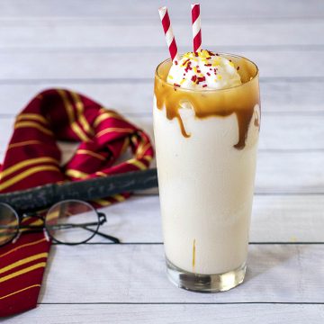 A butterbeer milkshake in front of a Gryffindor tie, a wand and a pair of glasses