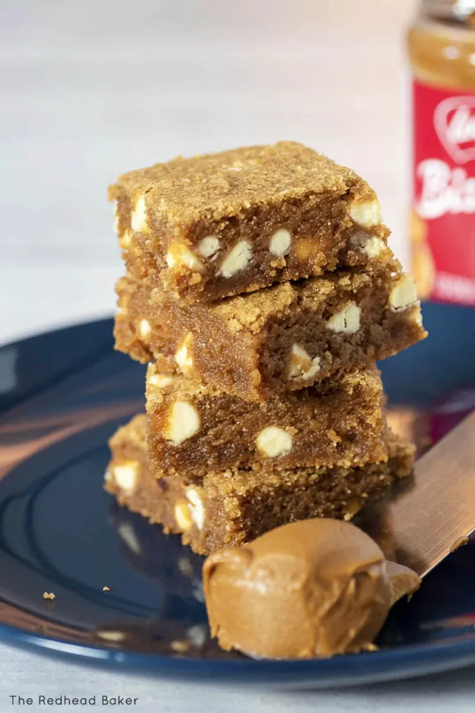 A stack of blondies on a blue plate with a spatula-full of cookie butter spread