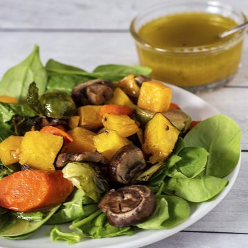 Roasted fall veggie salad on a white plate in front of a dish of cider vinaigrette