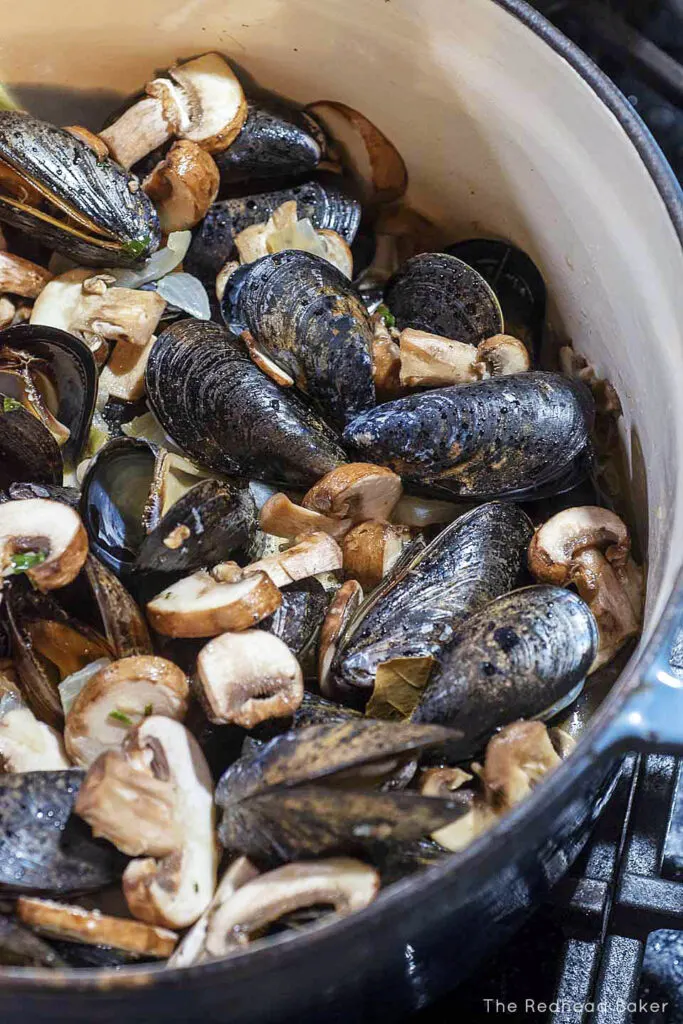 A Dutch oven filled with mussels, mushrooms, and chopped onion