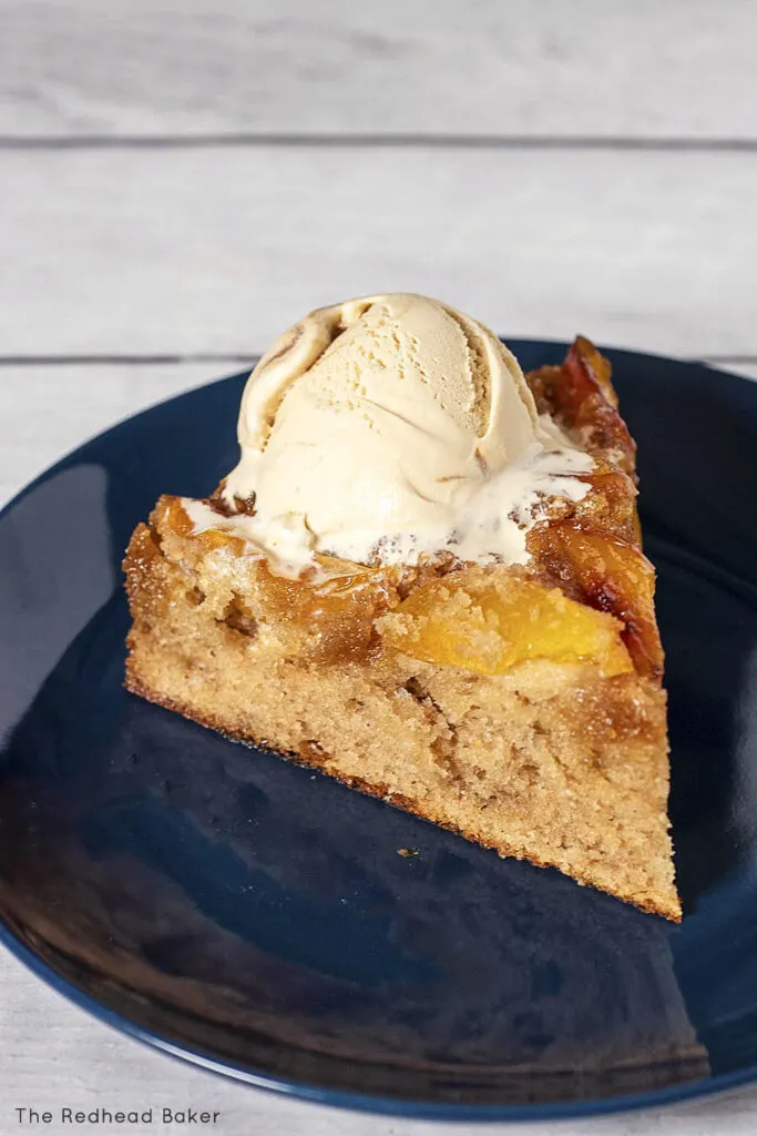 A slice of peach upside-down cake on a blue plate, topped with a scoop of caramel ice cream
