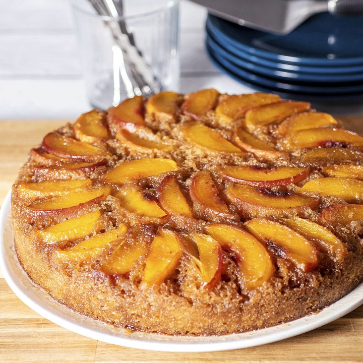 Peach upside down cake on a white serving plate, on top of a wooden cutting board