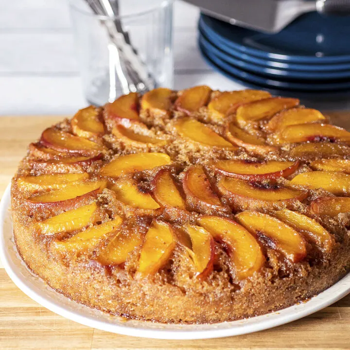 Peach upside down cake on a white serving plate, on top of a wooden cutting board