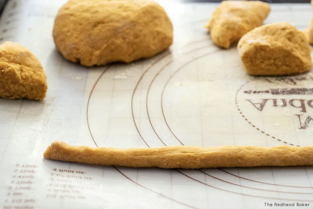 A rope of gnocchio dough on a pastry mat, in front of other lumps of dough