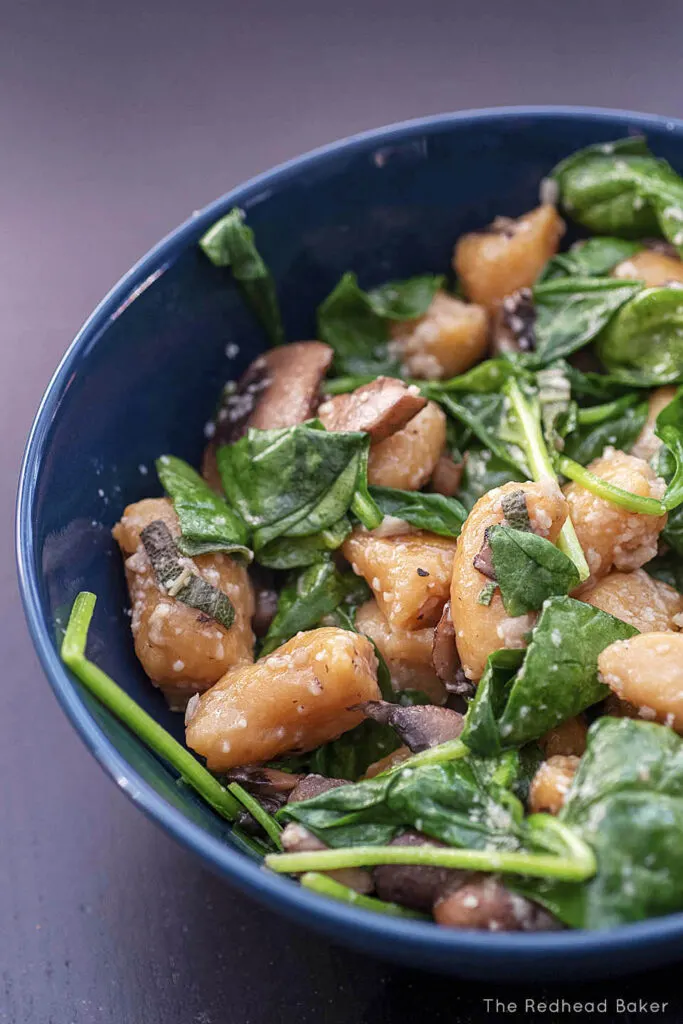 A bowl of pumpkin gnocchi with spinach, mushrooms, and parmesan cheese